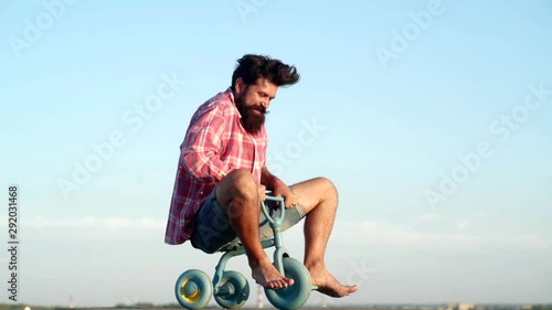 Crazy funny man rides a bike on sky background. Funny man having fun on children bicycle. Hipster with funny face. Different ages. Funny crazy man.