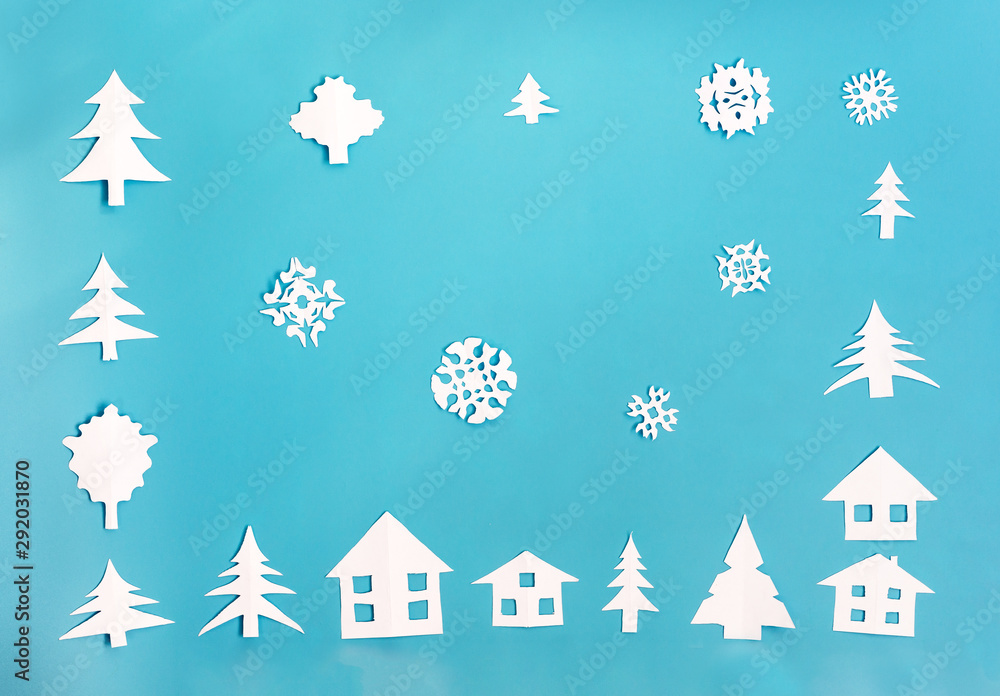 White paper figures of houses, Christmas trees and snowflakes on blue background