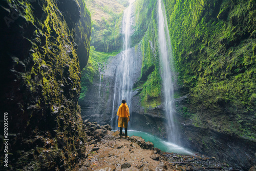 A happy tourist man watching Madakaripura Waterfall. The tallest waterfall in Java Island. Nature landscape background of travel trip and holidays vacation in Indonesia. Adventure lifestyle. photo