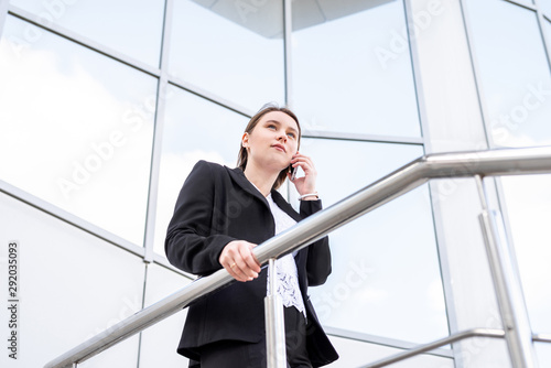 Beautiful caucasian business woman talking on cellphone while walking outdoor. City business woman working.