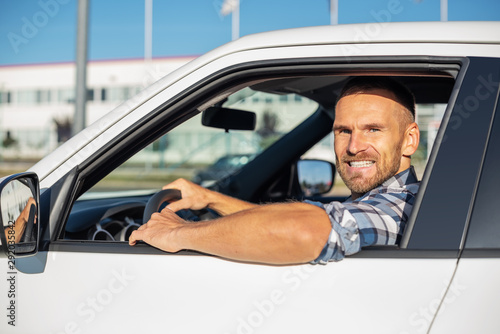 Attractive man driving a white car on a clear day. Buying or renting a car.