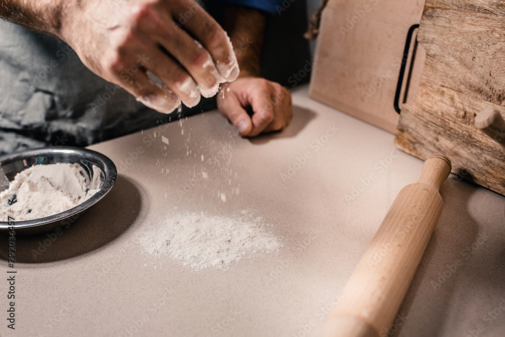 In a bakery, a Caucasian baker sprinkles flour on a table preparing a workplace for baking