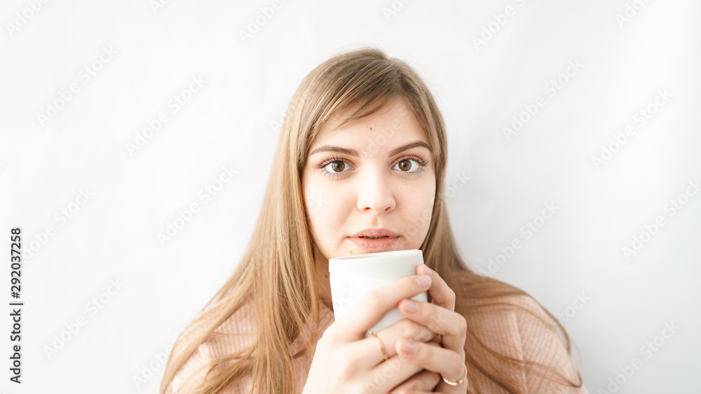 Funny school girl with mysterious look, wears a pink warm sweater, drinks coffee or tea, stands against white background with copy space for your promotional content Funny school girl with mysterious look, wears a pink warm sweater, drinks coffee or tea, stands against white background with copy space for your promotional content