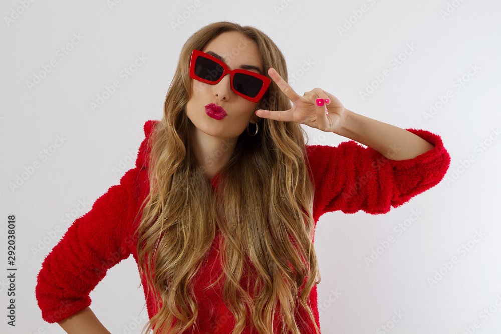 Young woman in red hoodie sweatshirt isolated on white background. Fashion and style concept. Peace sign gesture. Happy beautiful girl in red sunglasses. Make-up and beauty. Glamour model. Kiss face Young woman in red hoodie sweatshirt isolated on white background. Fashion and style concept. Peace sign gesture. Happy beautiful girl in red sunglasses. Make-up and beauty. Glamour model. Kiss face