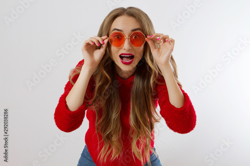 Closeup excited screaming young woman. shock, Shocked girl in red hoodie. Wow, surprised female. Fashion sweatshirt isolated on white background, face in red sunglasses. Beautiful, selective focus