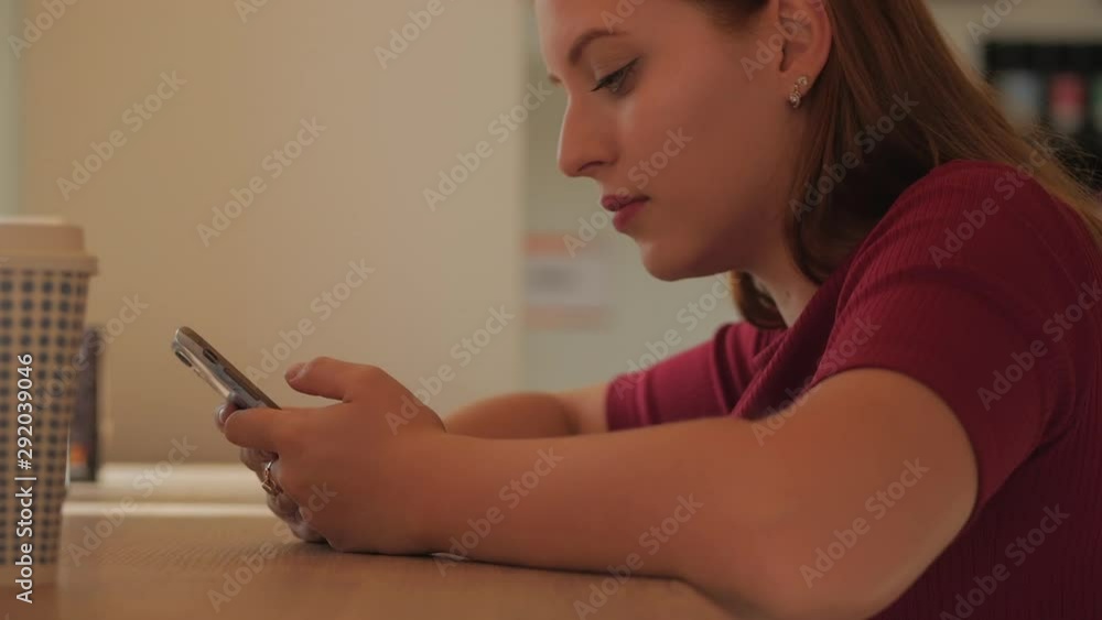 Young woman is sitting in a cafe and typing on a mobile phone. Concept of online stores. Young woman is sitting in a cafe and typing on a mobile phone. Concept of online stores.