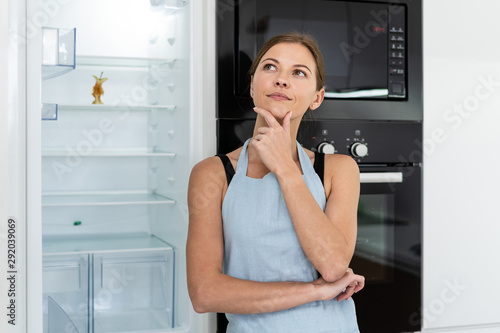 Young adult woman standing near refrigerator with apple