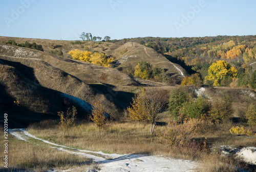 Chalk hills with paths, overgrown with fresh green grass and trees, сretaceous cliffs on a clear blue sky background