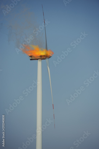 Eco power windturbine at sunny day under fire. Fire flames and black smoke escaping outside.