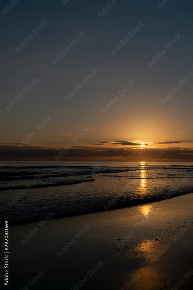 Oceanbeach as sun is on horizon creating golden glow across sea to beach still in dark of morning.