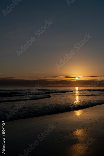 Oceanbeach as sun is on horizon creating golden glow across sea to beach still in dark of morning.