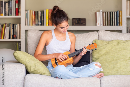 Fotografía young girl playing ukulele sitting in a sofa at home