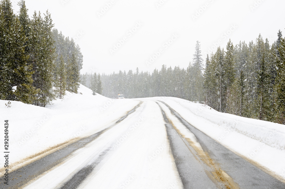 Forest road in the mountains durign a heavvy snowfall. A coming snowplough is visible in distance. Forest road in the mountains durign a heavvy snowfall. A coming snowplough is visible in distance.