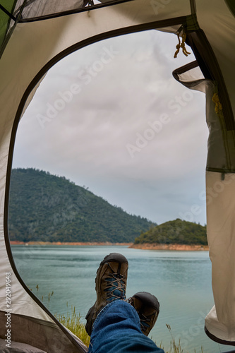 Cloudy landscape view of hiking boots in a tent door with a mountain lake in the background on a camping trip.