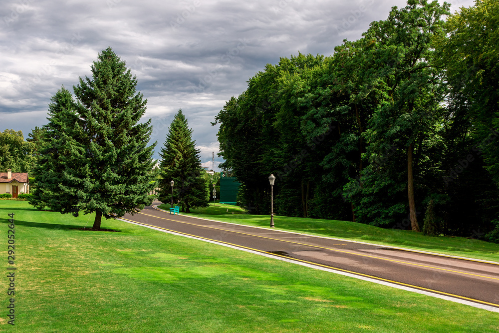 asphalt road with yellow marking of the bike path in the park with green grass and trees lit by sunlight after rain with a cloudy sky. asphalt road with yellow marking of the bike path in the park with green grass and trees lit by sunlight after rain with a cloudy sky.