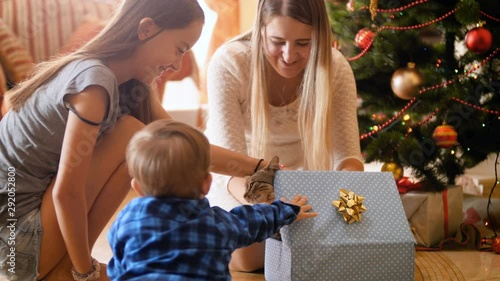 4k footage of happy family opens Christmas gifts and presents. Cute little kitten walking out of the box. Family having good time and fun on winter holidays and celebrations. photo