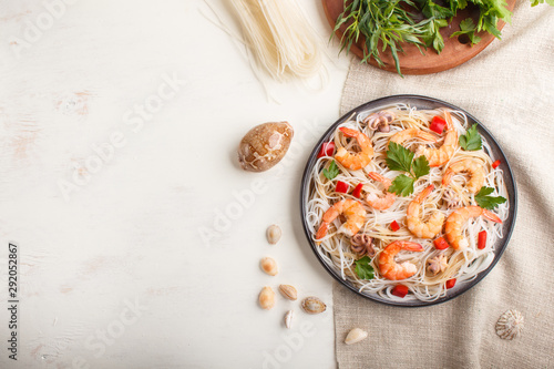 Rice noodles with shrimps or prawns and small octopuses on gray ceramic plate on a white wooden background. Top view.