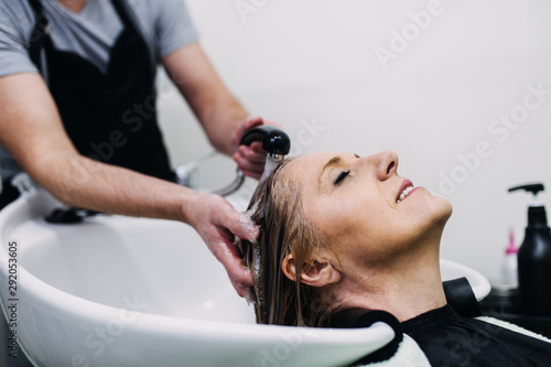 Hairdresser washing hair of a beautiful mature woman in hair salon.