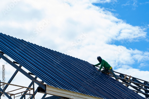 Roofer worker in protective uniform wear and gloves, using air or pneumatic nail gun and installing asphalt shingle on top of the new roof,Concept of residential building under construction. photo