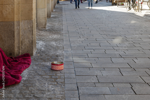 Homeless or beggar sleep or hide under red blanket at corner of building along street and set a circle tin box for money charity in old town Düsseldorf. Germany. Inequality problem in big city. 