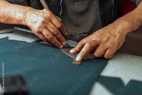Hands of an old and experienced worker in the handmade shoe industry, performing cutting tasks on genuine patterned leather, on a glass surface, the beginning of footwear production.