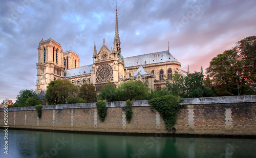 Notre Dame Cathedral in Paris France just before sunrise. Photo shows the banks of the Seine river in the foreground.