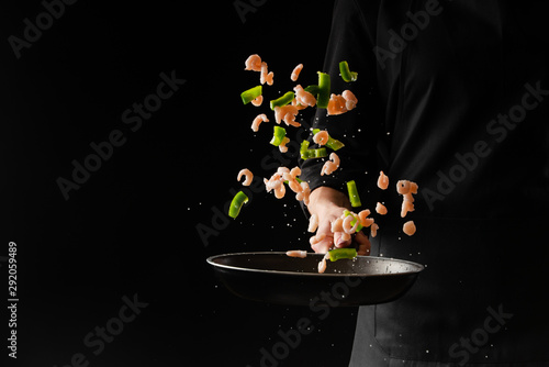 Chef cooks shrimps with green herbs in a pan on a black background. Seafood and healthy food.