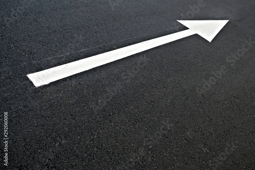 White arrow gives traffic direction, white reflective paint on a black road surface. © Daguimagery