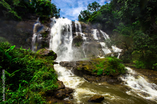 Natural blurred background of waterfalls, fast-flowing currents and water droplets from the wind blowing among the rocks and surrounded by big trees, spontaneous beauty