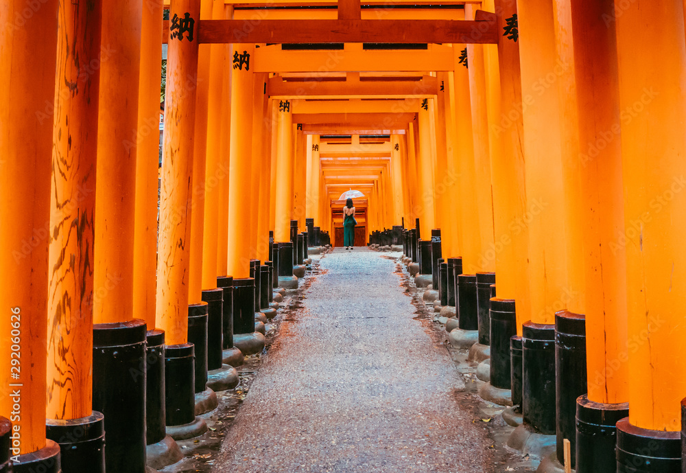 One of the main highlight in Japan and the most popular destination. This is a corridor made of tori gates. Orange tunnel. In the end standing lady, she is wearing dress and holding white umbrella. One of the main highlight in Japan and the most popular destination. This is a corridor made of tori gates. Orange tunnel. In the end standing lady, she is wearing dress and holding white umbrella.