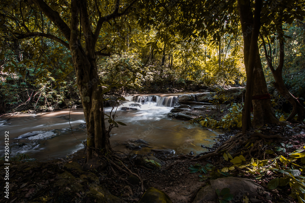 Natural blurred background of waterfalls, fast-flowing currents and water droplets from the wind blowing among the rocks and surrounded by big trees, spontaneous beauty