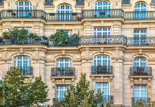 Street view of an old, elegant residential building facade in Paris, with ornate details in the stone walls, french doors and wrought iron railings on the balconies. © Cheryl Ramalho