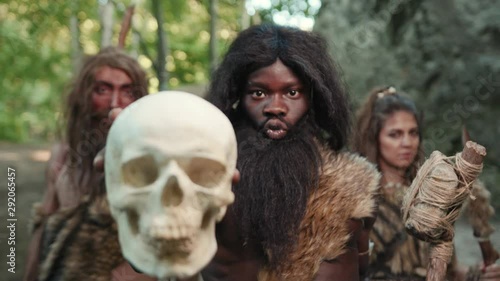 Neanderthal tribe of dangerous hunter-gatherers cannibalists showing bald human skull casting hypnotic spell with grow sounds. Cannibalists in prehistoric period.