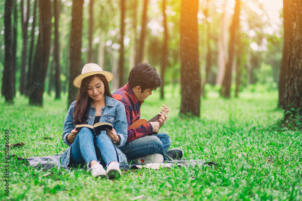 A young couple reading book and playing ukulele while sitting in the woods A young couple reading book and playing ukulele while sitting in the woods