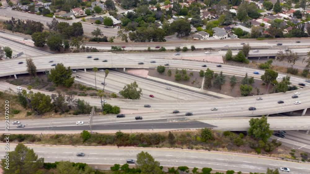 4K. Aerial Los Angeles freeway shot. Crossing motorway lanes with driving vehicles on them are in frame. Many autos move fast in different directions. Suburban houses are behind the highway 4K. Aerial Los Angeles freeway shot. Crossing motorway lanes with driving vehicles on them are in frame. Many autos move fast in different directions. Suburban houses are behind the highway