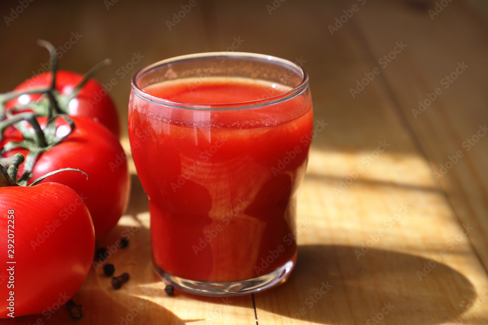red tomato juice. fresh tomato juice in a glass glass and ripe fruit on a light wooden Board. close up. beautiful shadow and light. red tomato juice. fresh tomato juice in a glass glass and ripe fruit on a light wooden Board. close up. beautiful shadow and light.