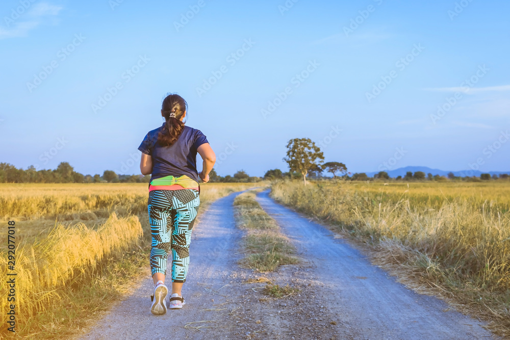 Back view of woman running and exercising on the path through the rice fields in the evening.