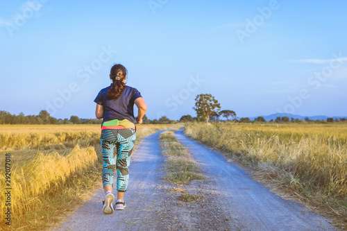Back view of woman running and exercising on the path through the rice fields in the evening. © JinnaritT
