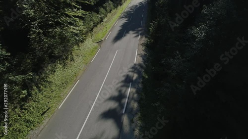 Fly down aerial with car following the the road that leeds you through Triglav National park, view with beautiful green pine trees. Yellow sunlight above tree. Beautiful sunflair in the screen photo