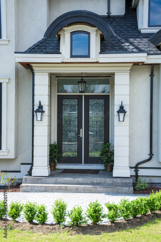 An entrance of a luxury house decorated with small trees in front.