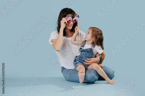 Mother and daughter playing with happy birthday glasses over blue background