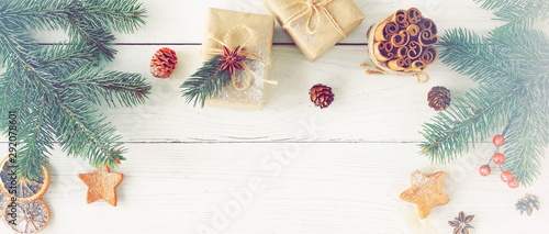 Christmas background banner with fir twigs, gifts, red berries, cones, sinnamon sticks and Xmas decor on white wooden background top view. vintage toned. Copy space