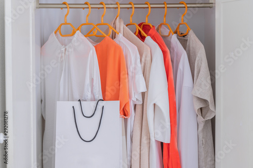 Collection of Coral and White colour clothes hanging on rack in wardrobe in dressing room and white shopping bags. Fashion concept background. © vasanty