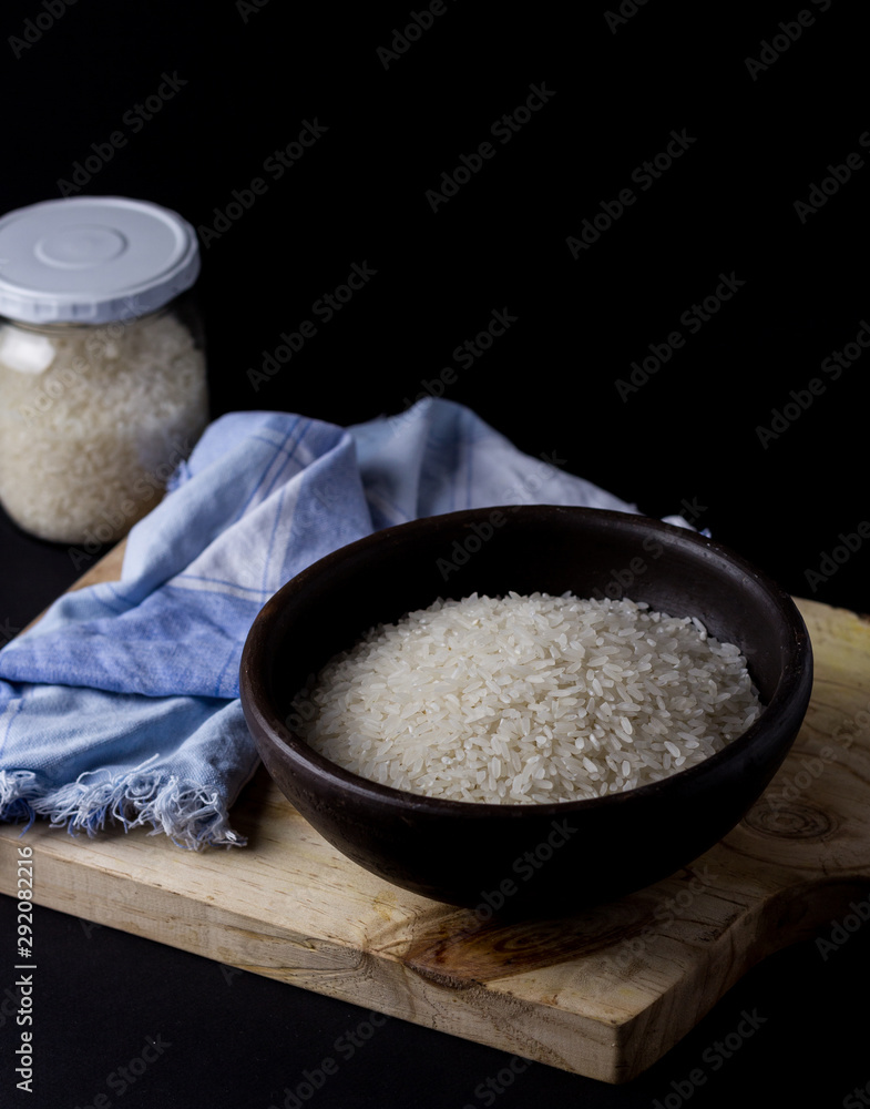 Uncooked rice in clay bowl on a wooden table with black background.