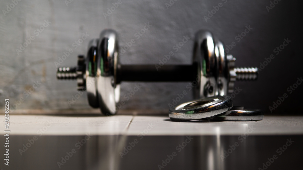 Fototapeta premium Metal dumbbell equipment with wall background rolling on the floor.