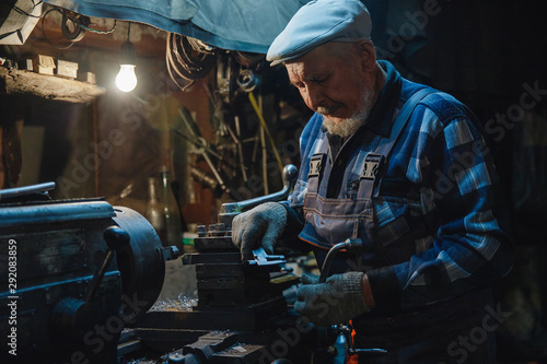 Senior elderly male turner handles metal on machine. Concept pension worker industrial, workplace