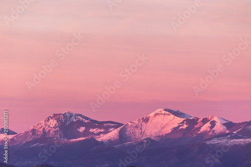 Mountain top covered by snow with a beautiful orange sky on the background