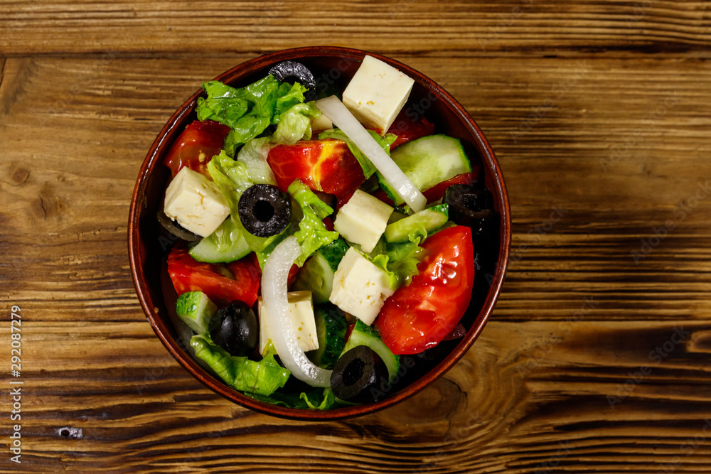 Greek salad with fresh vegetables, feta cheese and black olives on wooden table. Top view