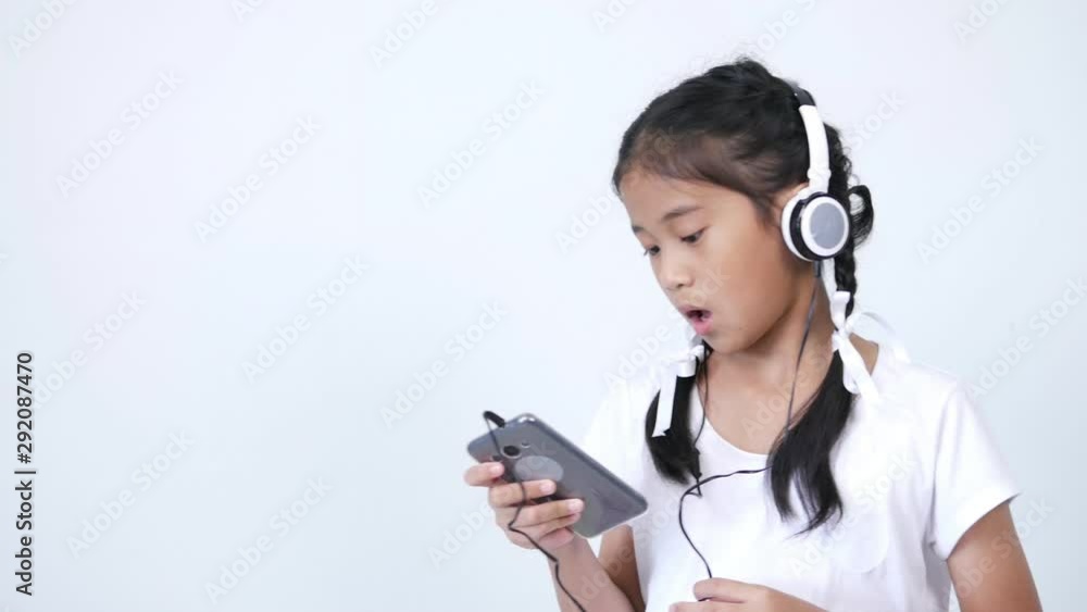 The girl looks cute and wears a white shirt and a braid tied with a white ribbon using the headphones, listening to music from social media on smartphone, singing softly and rocking along the song. The girl looks cute and wears a white shirt and a braid tied with a white ribbon using the headphones, listening to music from social media on smartphone, singing softly and rocking along the song.