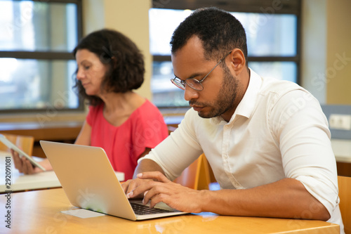 Serious male Latin trainee working in computer class. People sitting at desks and using laptops in classroom. Training course concept photo